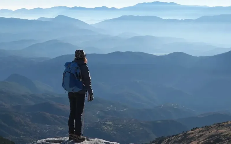 A lone walker looking out over layered blue mountains